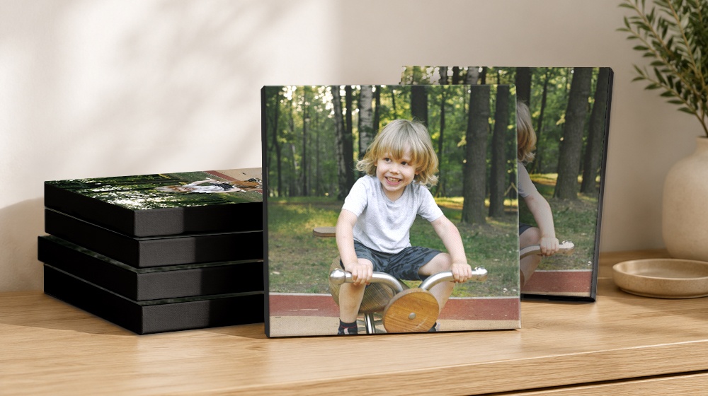 Canvas prints of a smiling child riding a wooden toy outdoors, displayed beside stacked canvases on