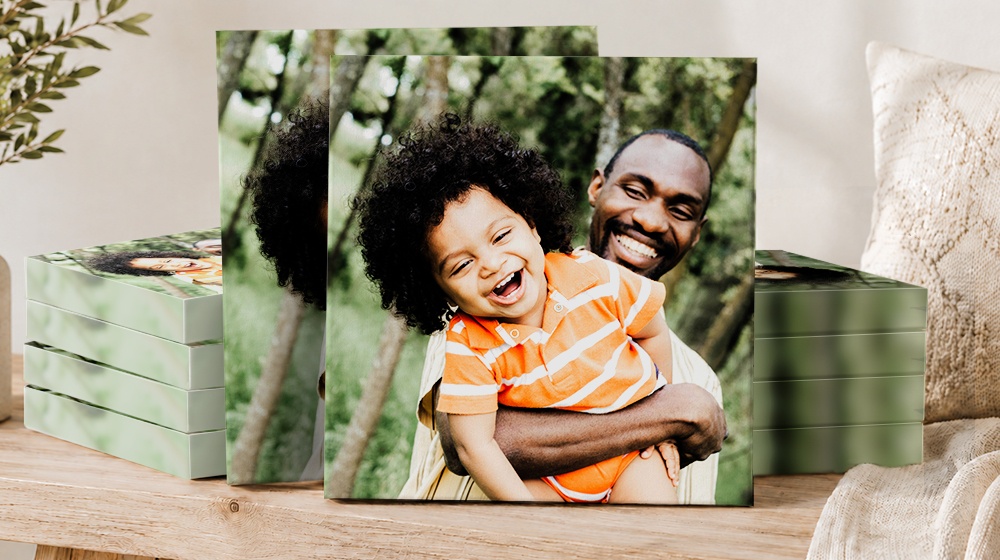 Canvas prints of a father hugging his smiling child, displayed beside stacked canvases.