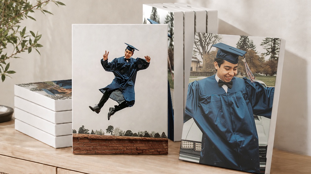 Graduation photo canvas prints displayed beside stacked canvases on a wooden table.