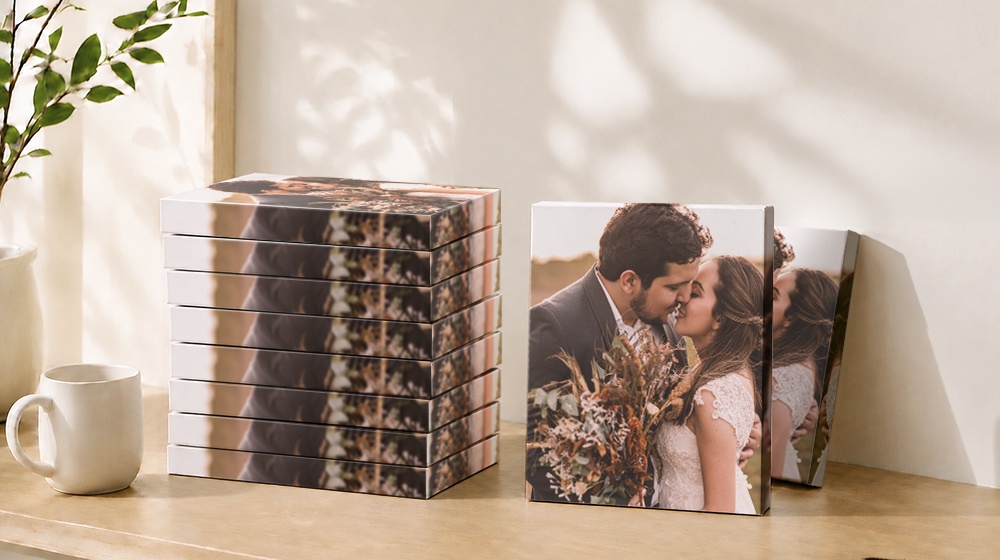 Wedding photo canvas prints displayed beside stacked canvases on a wooden table.