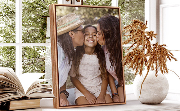 light wood floating framed canvas of two parents kissing their daughter on the cheek