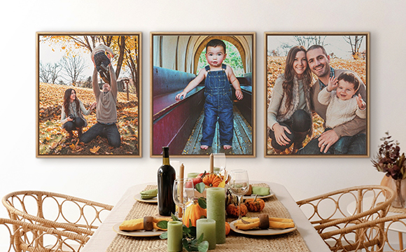 Three family photo canvas prints in natural wood floating frames above a dining table decorated with